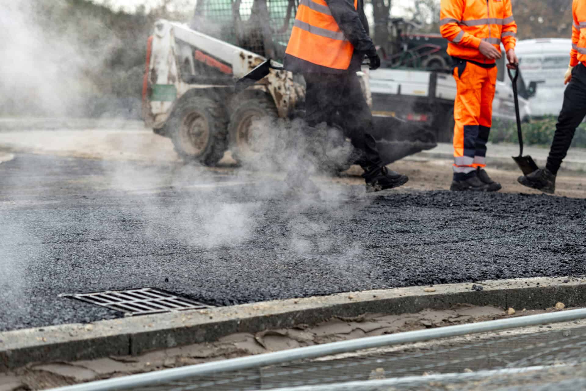 Street construction crew laying asphalt with steam rising on a bustling urban day in early morning light